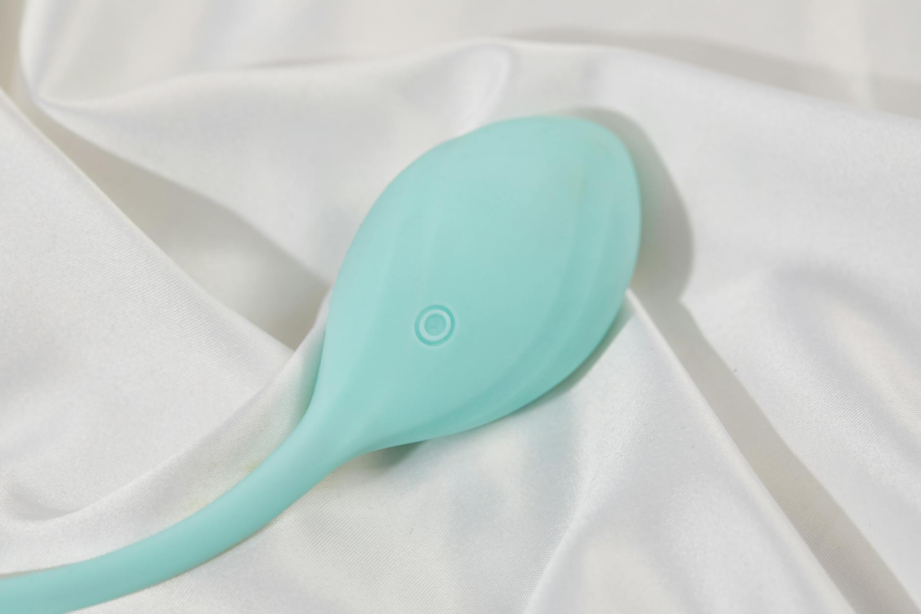 A teal suction vibrator on soft white silk fabric