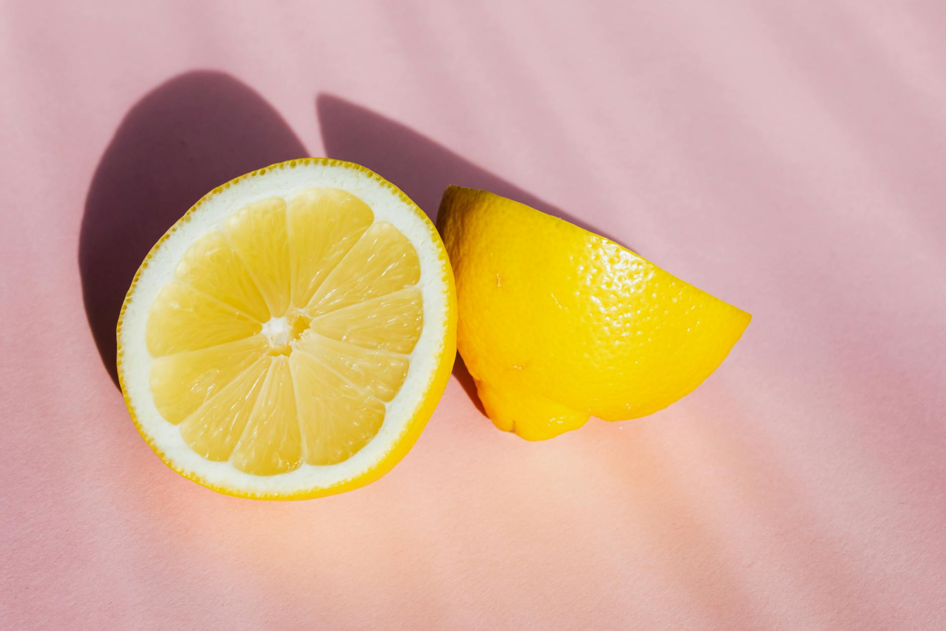 A close-up view of fresh lemon halves arranged on a pink surface in natural sunlight