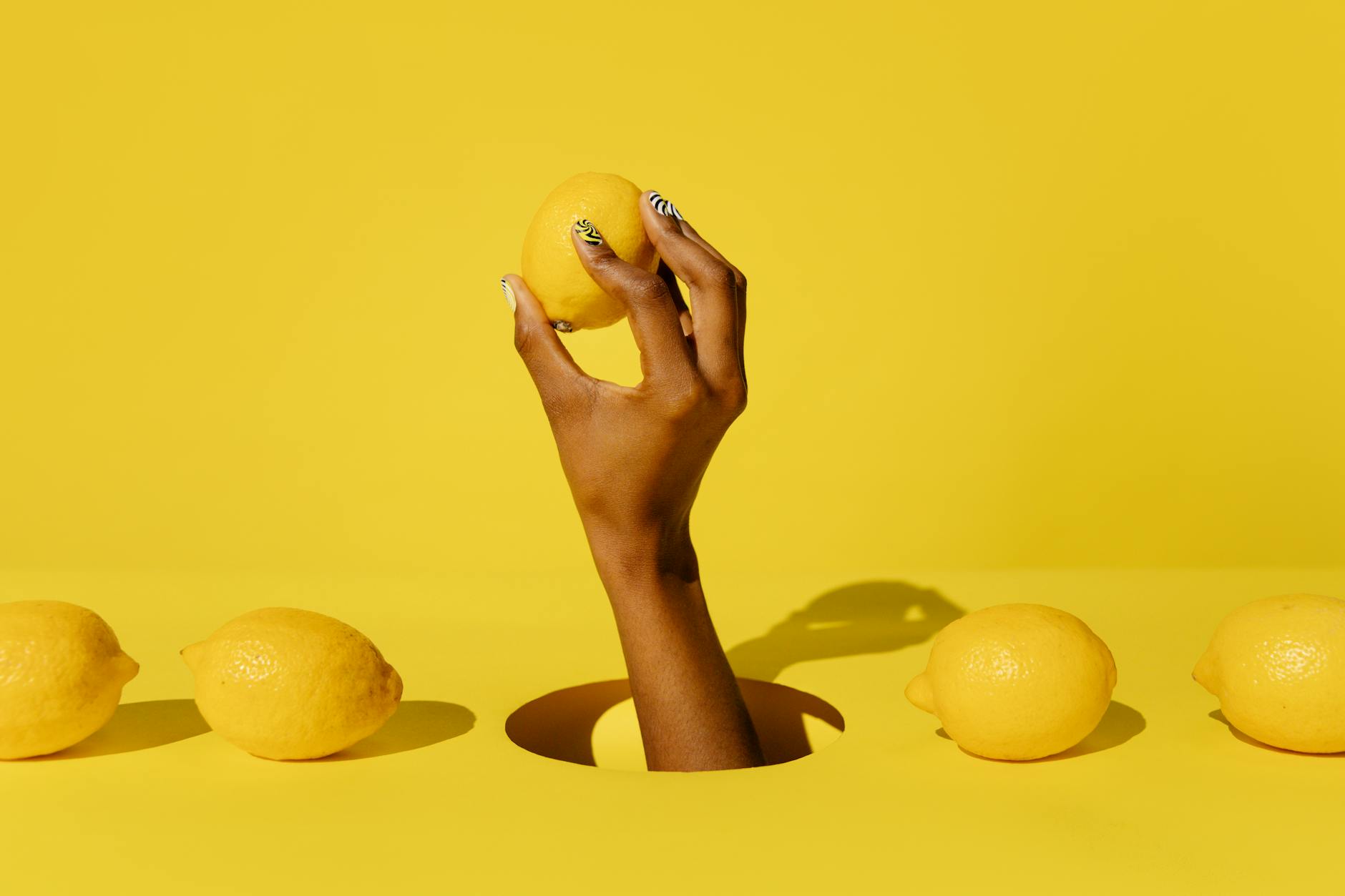 A hand holding a fresh lemon against a vivid yellow background, symbolizing the precision and natural feel of lemon vibrator design