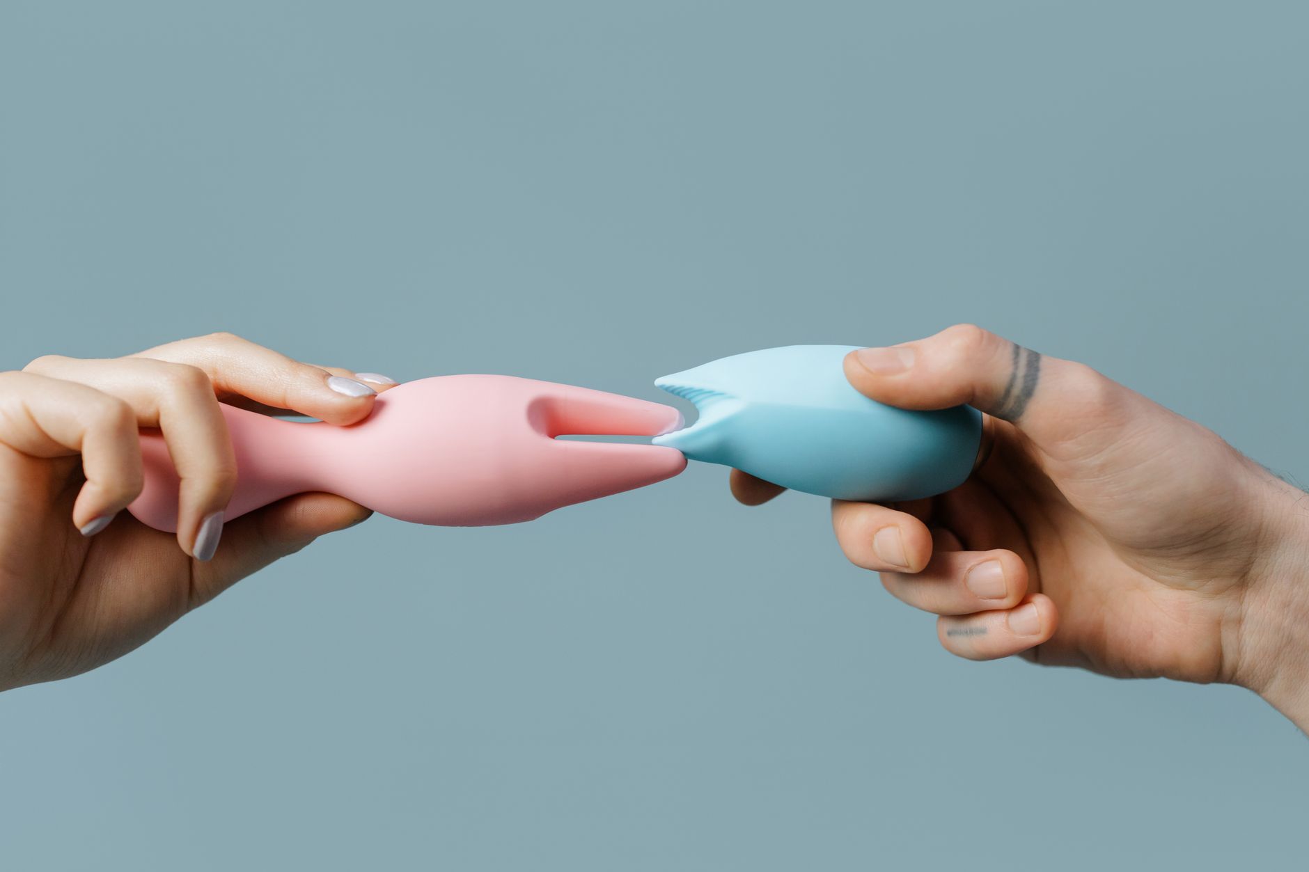 Hands holding pastel-colored silicone toys on a neutral background