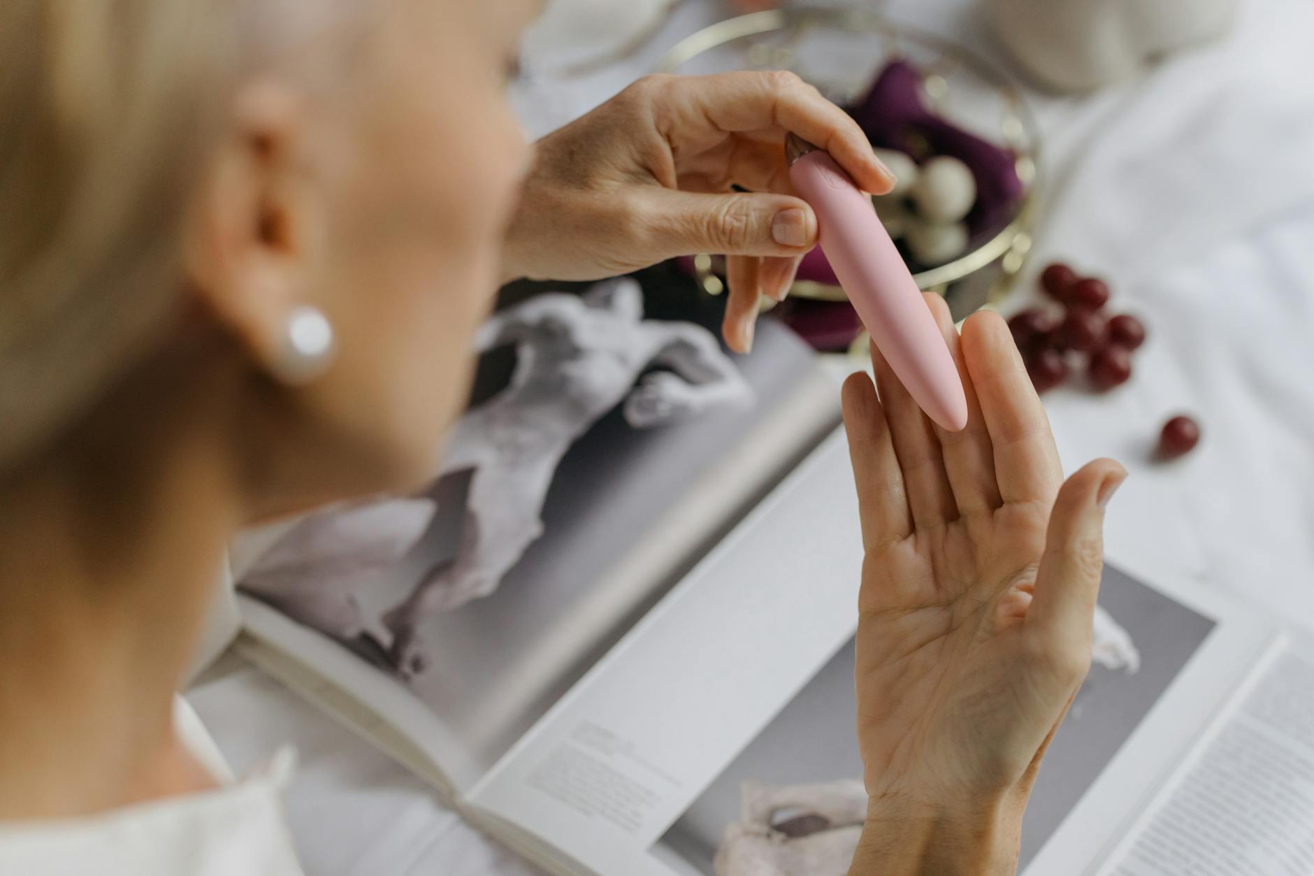 Close-up of a woman holding a pink vibrator with art books in the background.