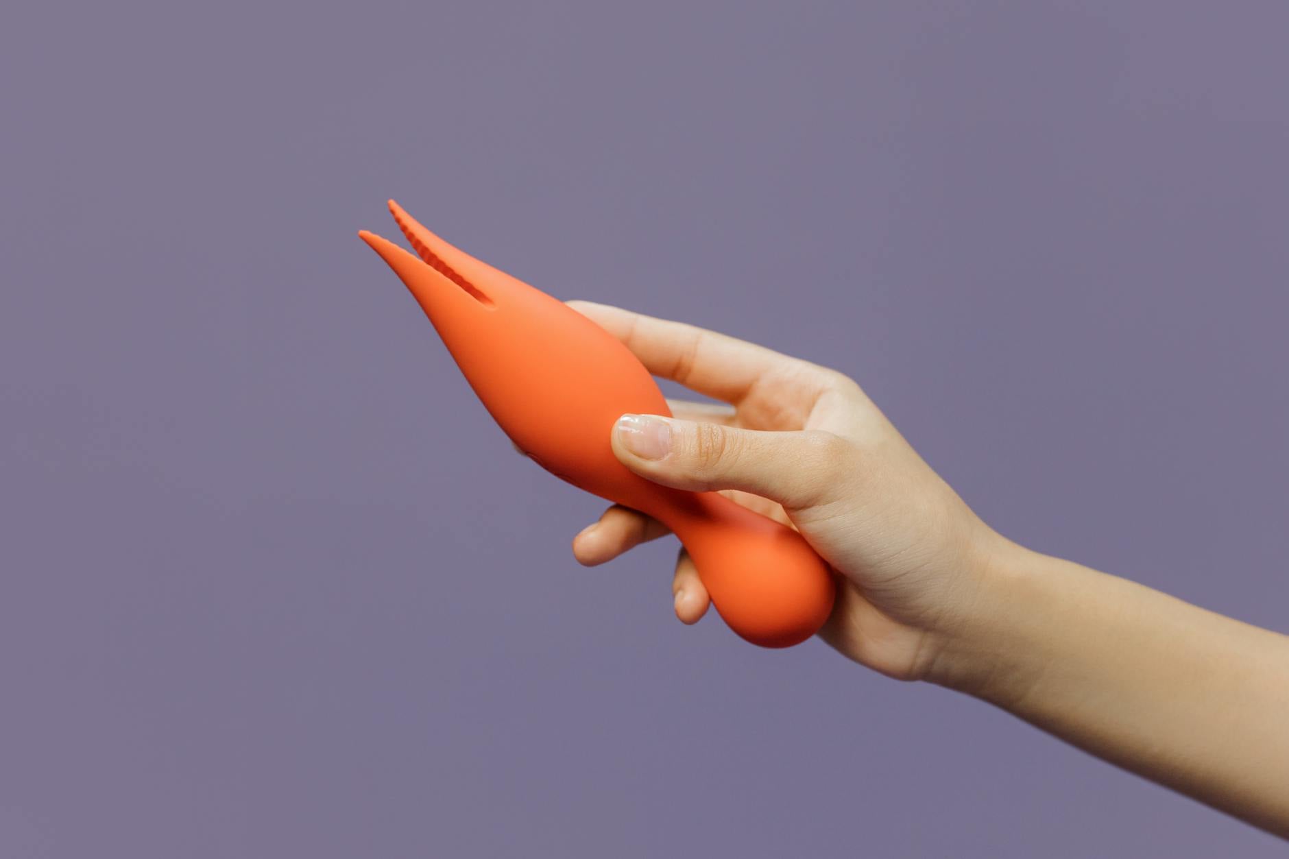 Close-up of hand holding a lemon-colored vibrator against a minimalistic purple backdrop, representing modern intimacy exploration