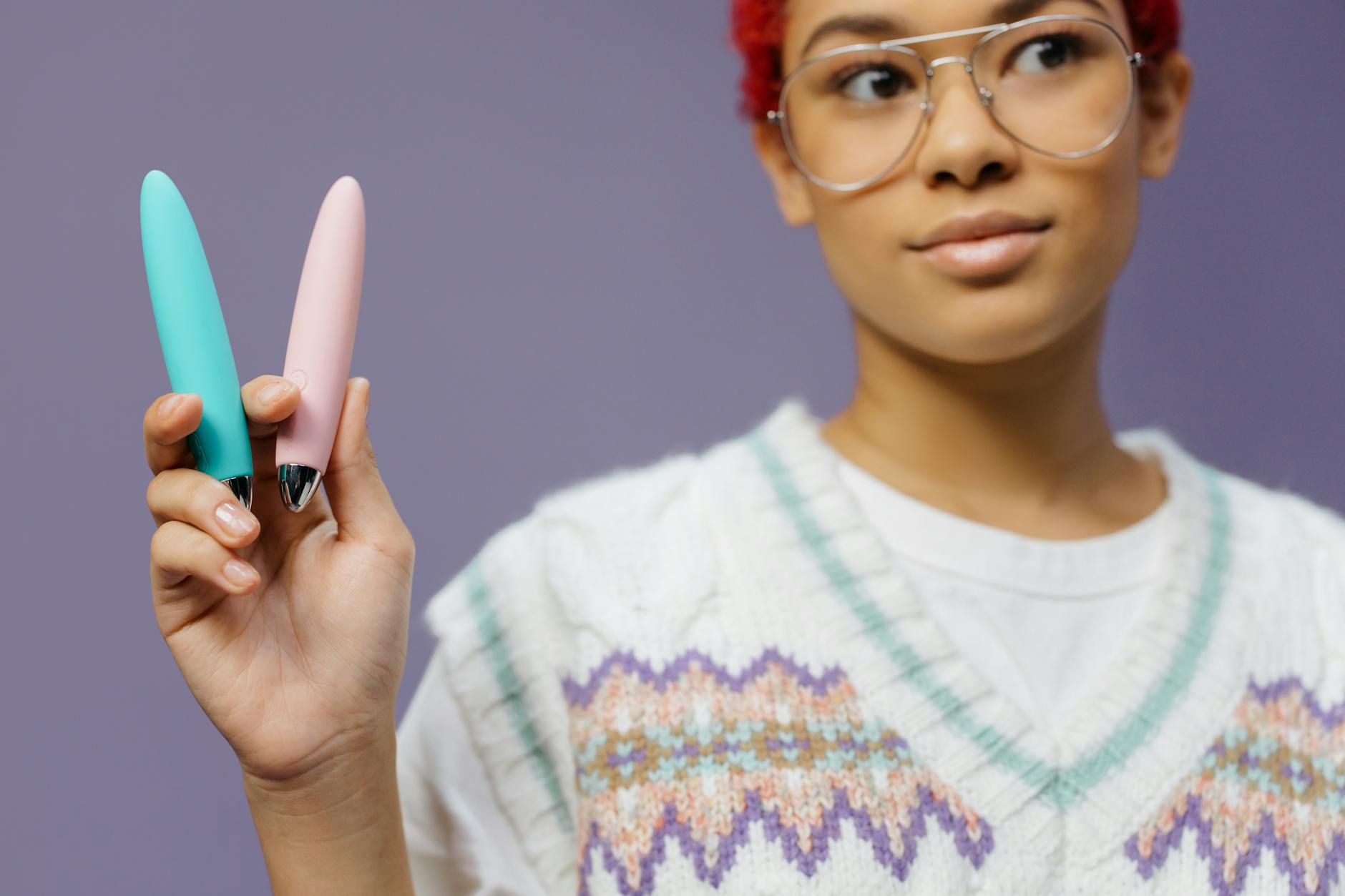 Woman holding colorful vibrators against a purple background, representing self-directed pleasure and recovery.