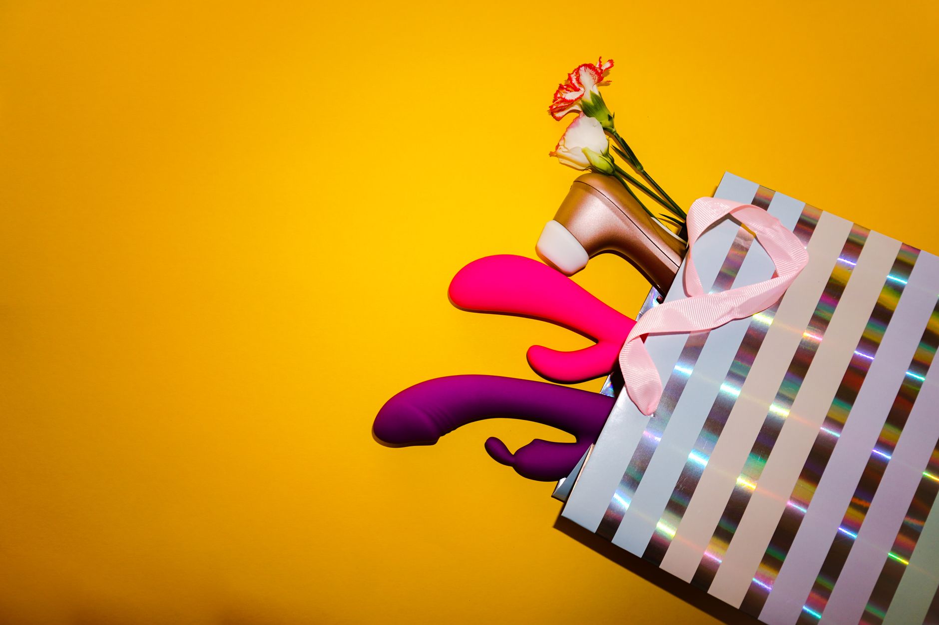 Colorful lemon vibrators with flowers in a holographic gift bag on a bright yellow background