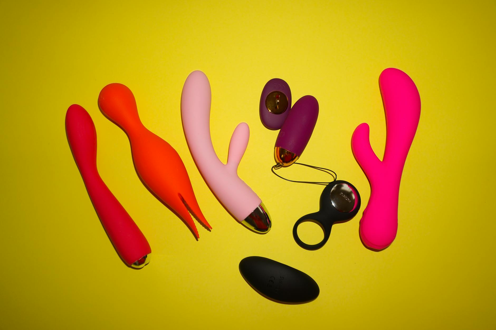 A hand reaching over a variety of colorful clitoral vibrators and toys arranged on a table