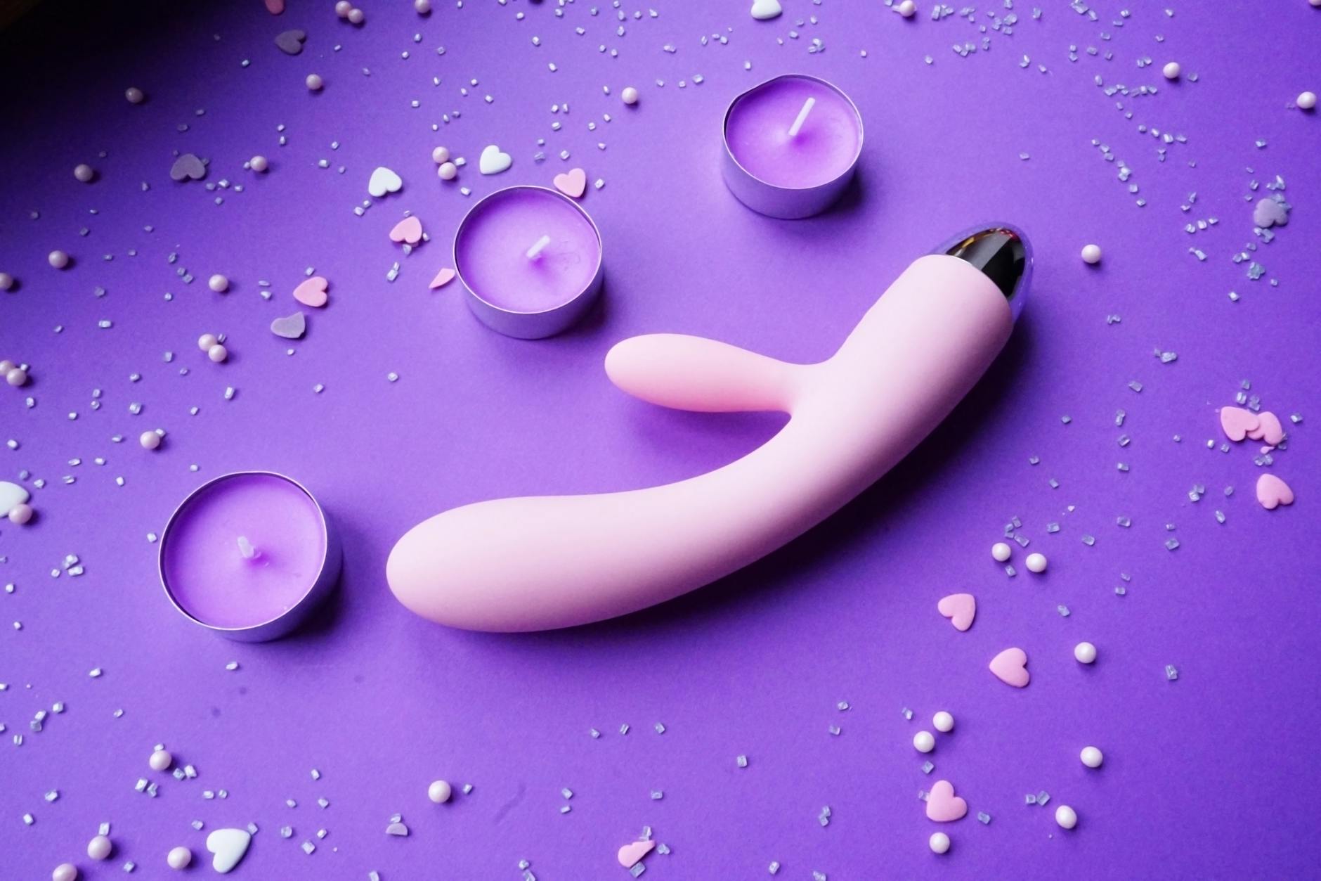 Pink lemon clitoral vibrator on purple background with heart confetti and candles
